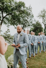 Load image into Gallery viewer, Groom in light blue suit reading vows with groomsmen in matching suits standing in a line outdoors.