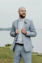 Load image into Gallery viewer, Man in a light blue suit standing by a body of water