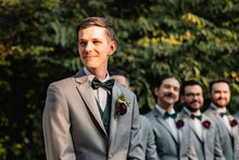 Load image into Gallery viewer, Man in a gray suit with a green bow tie standing outdoors with other men in similar suits.