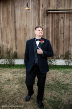 Load image into Gallery viewer, Man in a black suit standing in front of a wooden wall