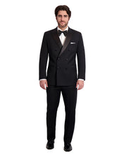 Load image into Gallery viewer, A man wearing a double-breasted, black tuxedo with a peak lapel and six button front. The tuxedo is designed by Ike Behar.